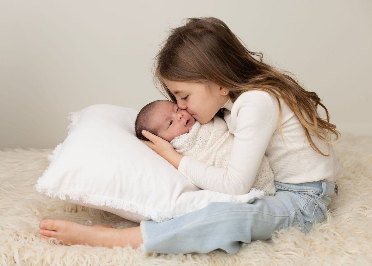 A tender moment shared between mother and baby lying on soft white pillows and plush carpet.