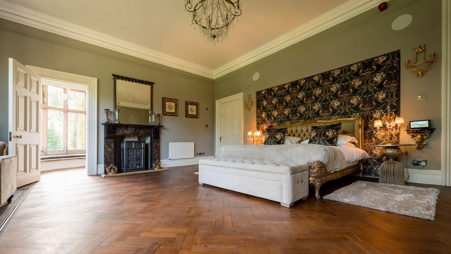 Panoramic view of a formal sitting room with chandelier and classic green wallpaper. Ellingham Hall