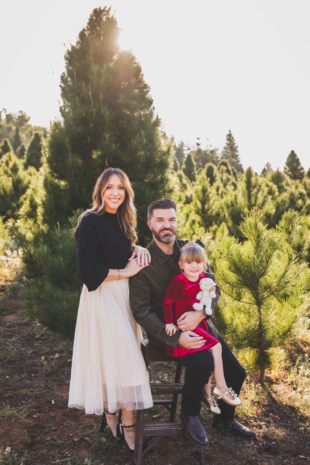 A family shares joyful moments together among evergreen trees at sunset in a Christmas tree farm setting.
