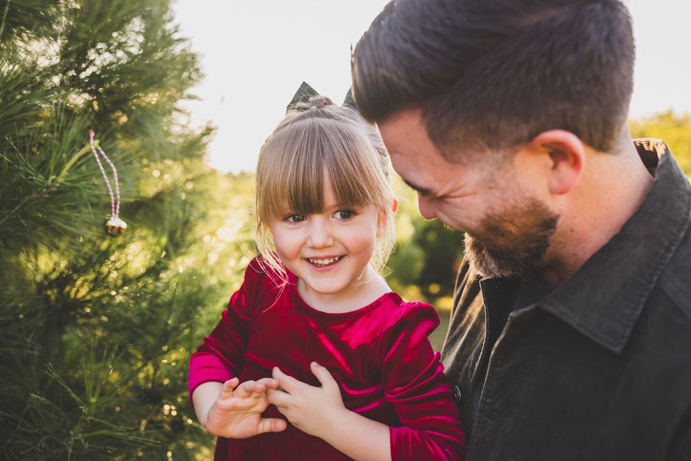 A couple shares a tender moment together in a sunlit outdoor setting wearing burgundy and black clothing.