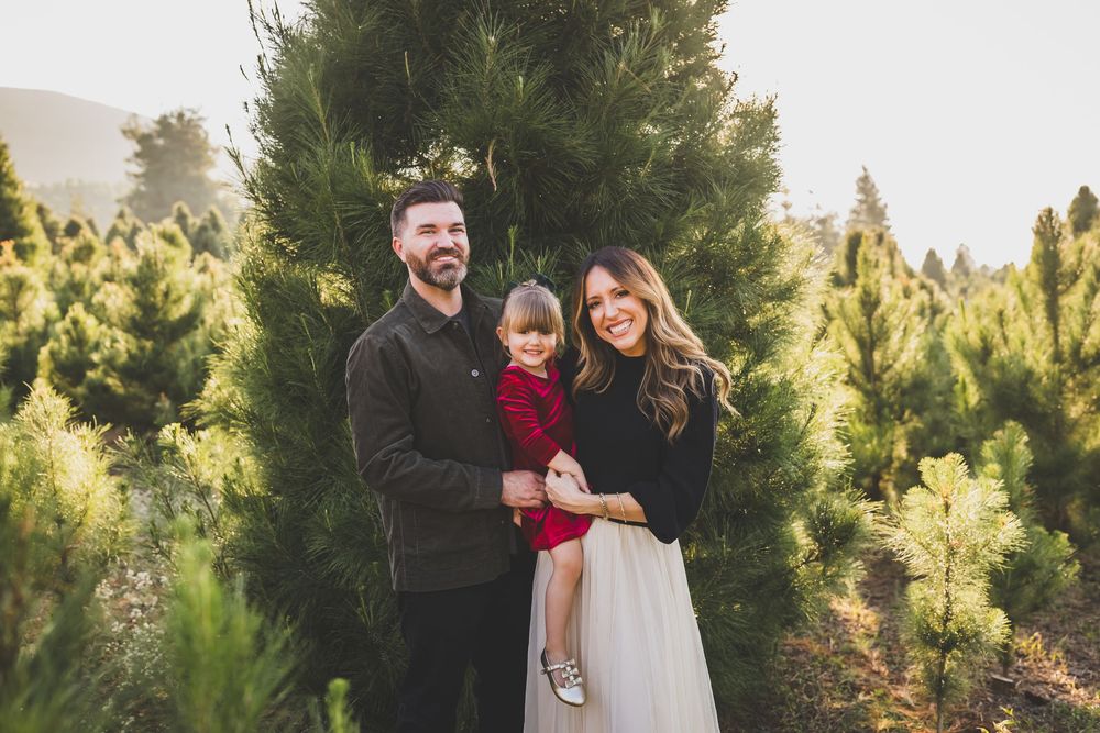 A family poses together at a Christmas tree farm surrounded by evergreen trees on a misty afternoon.