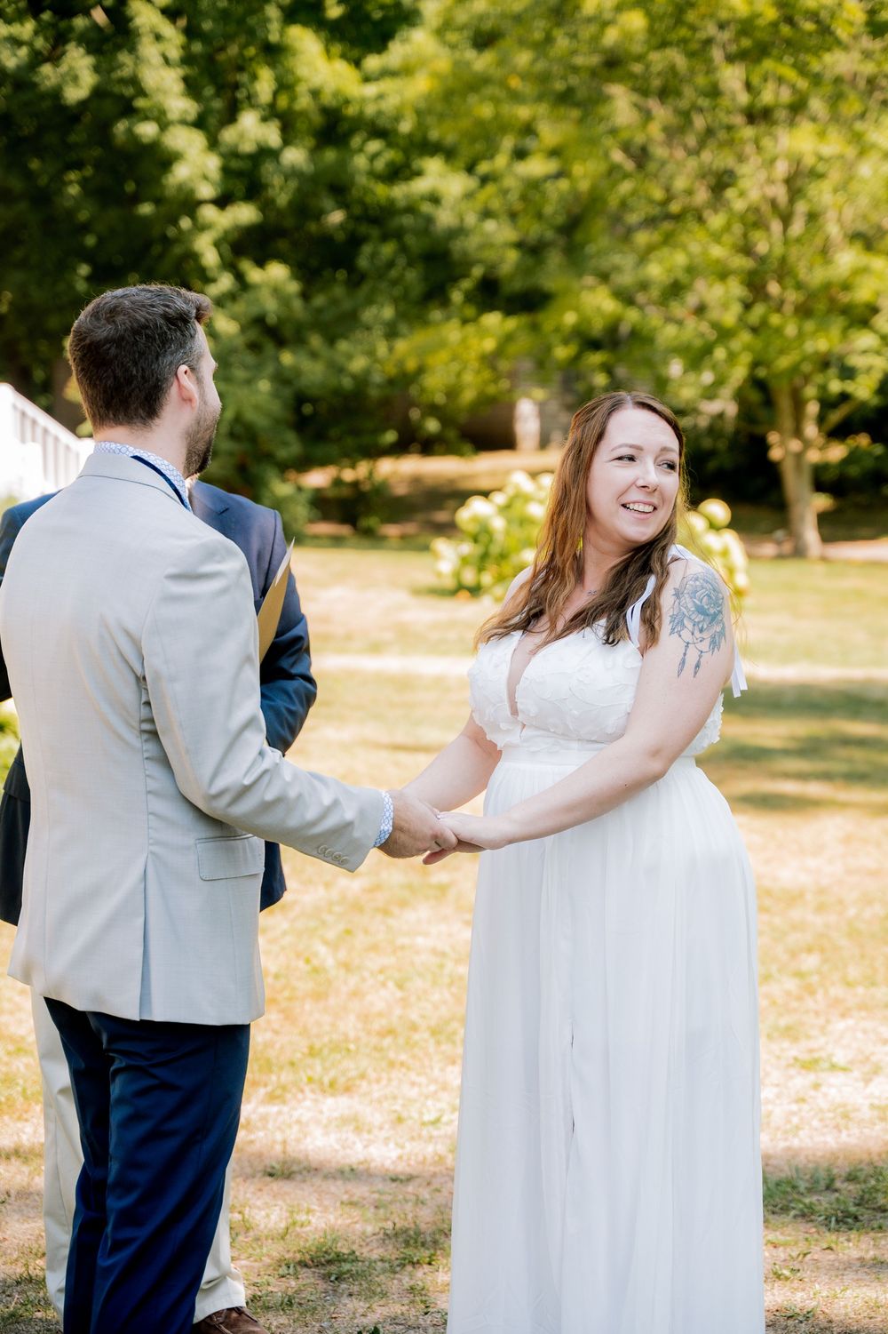 A couple in formal attire dances together in a sunny outdoor garden setting with autumn leaves on the ground.