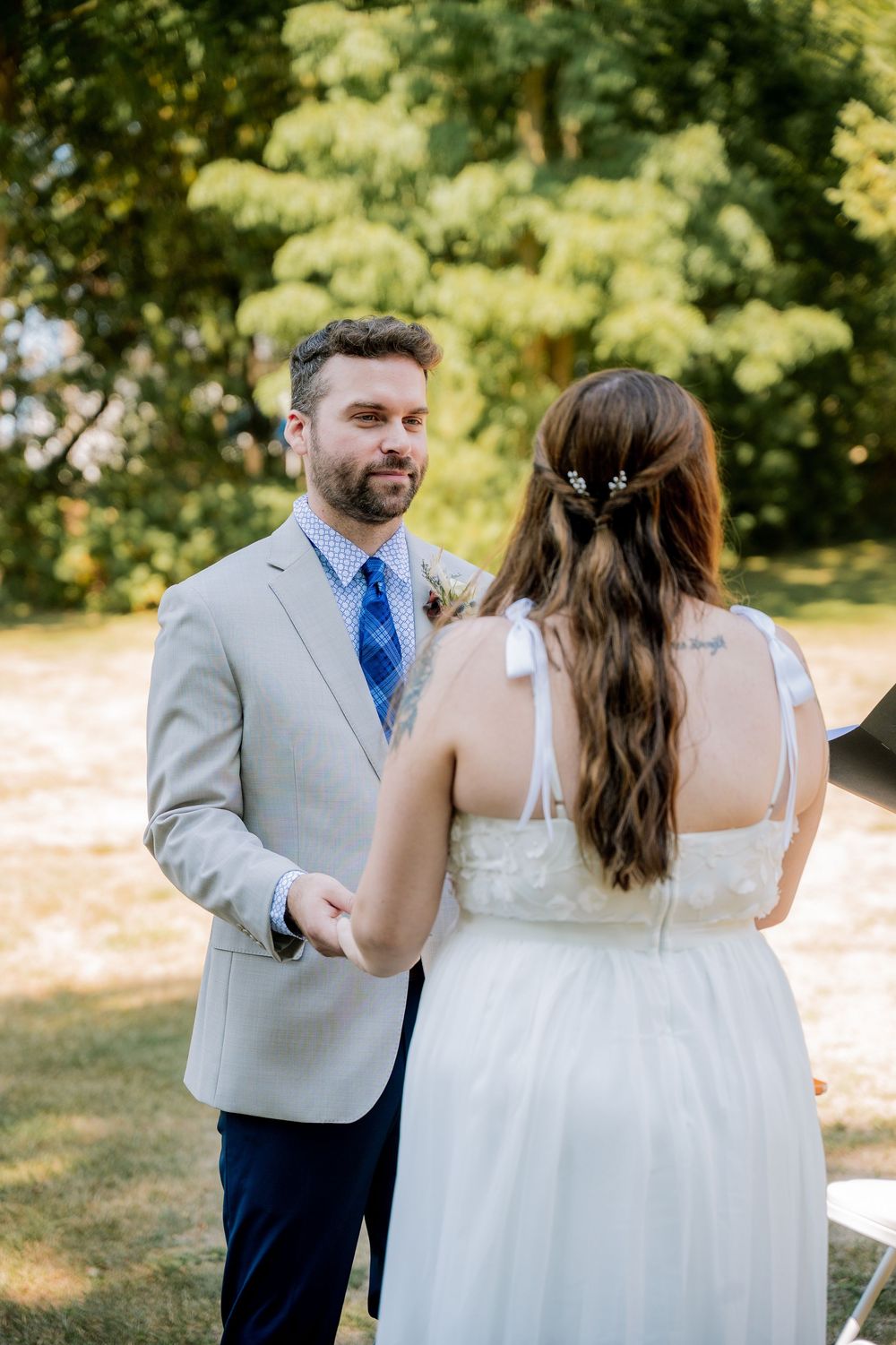 A couple shares an intimate moment in a sunny outdoor setting, with the person in gray and blue attire leading.