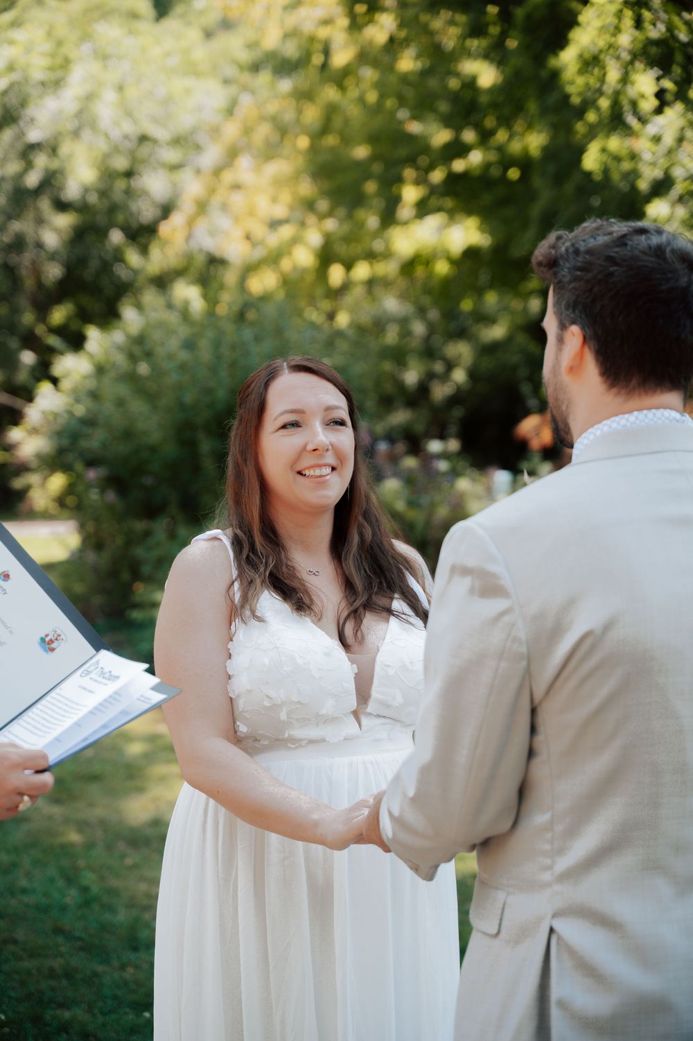 A couple shares a joyful moment during their outdoor wedding ceremony surrounded by lush greenery.