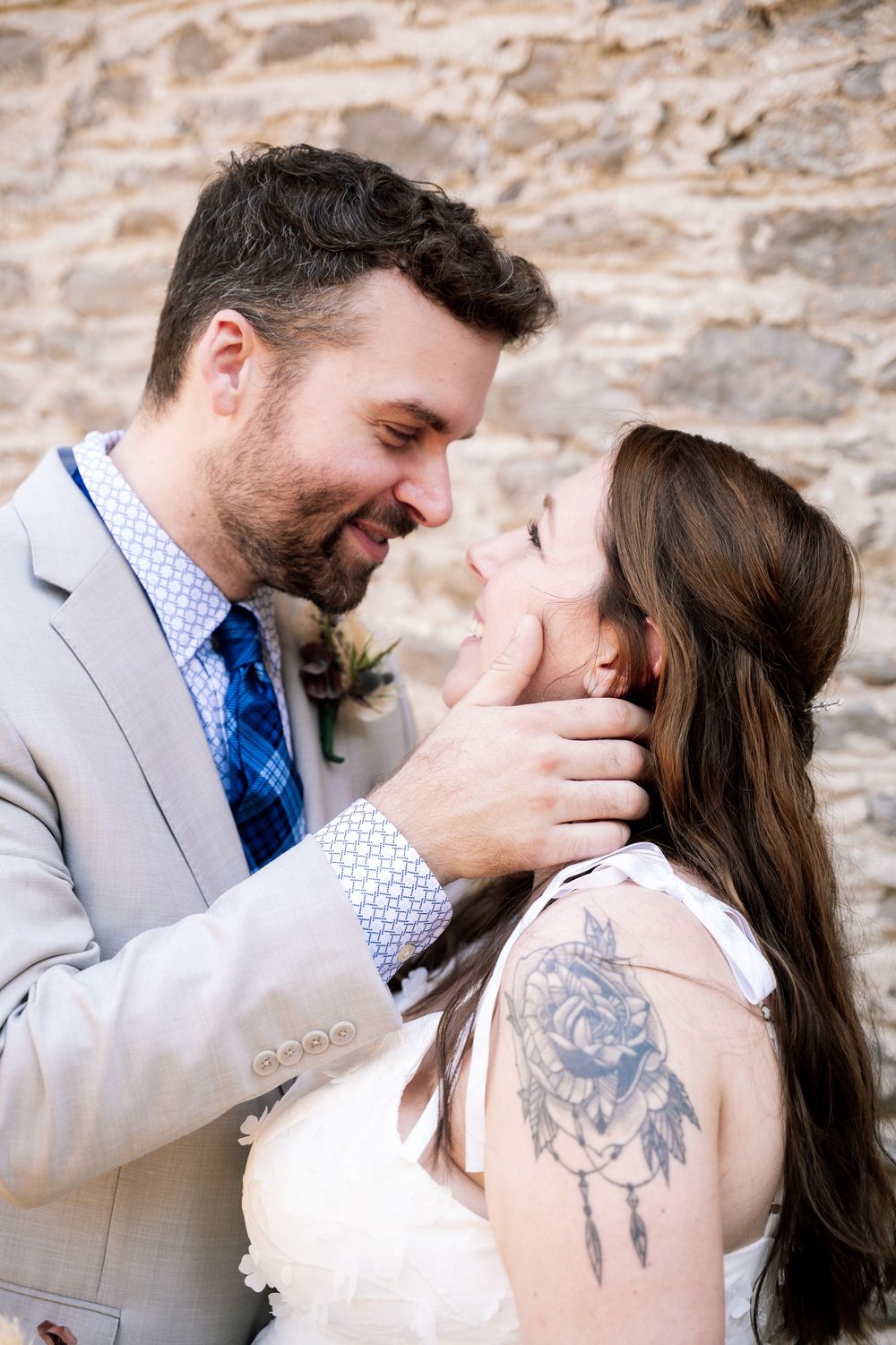 A couple shares an intimate moment against a stone wall backdrop during their wedding photoshoot.