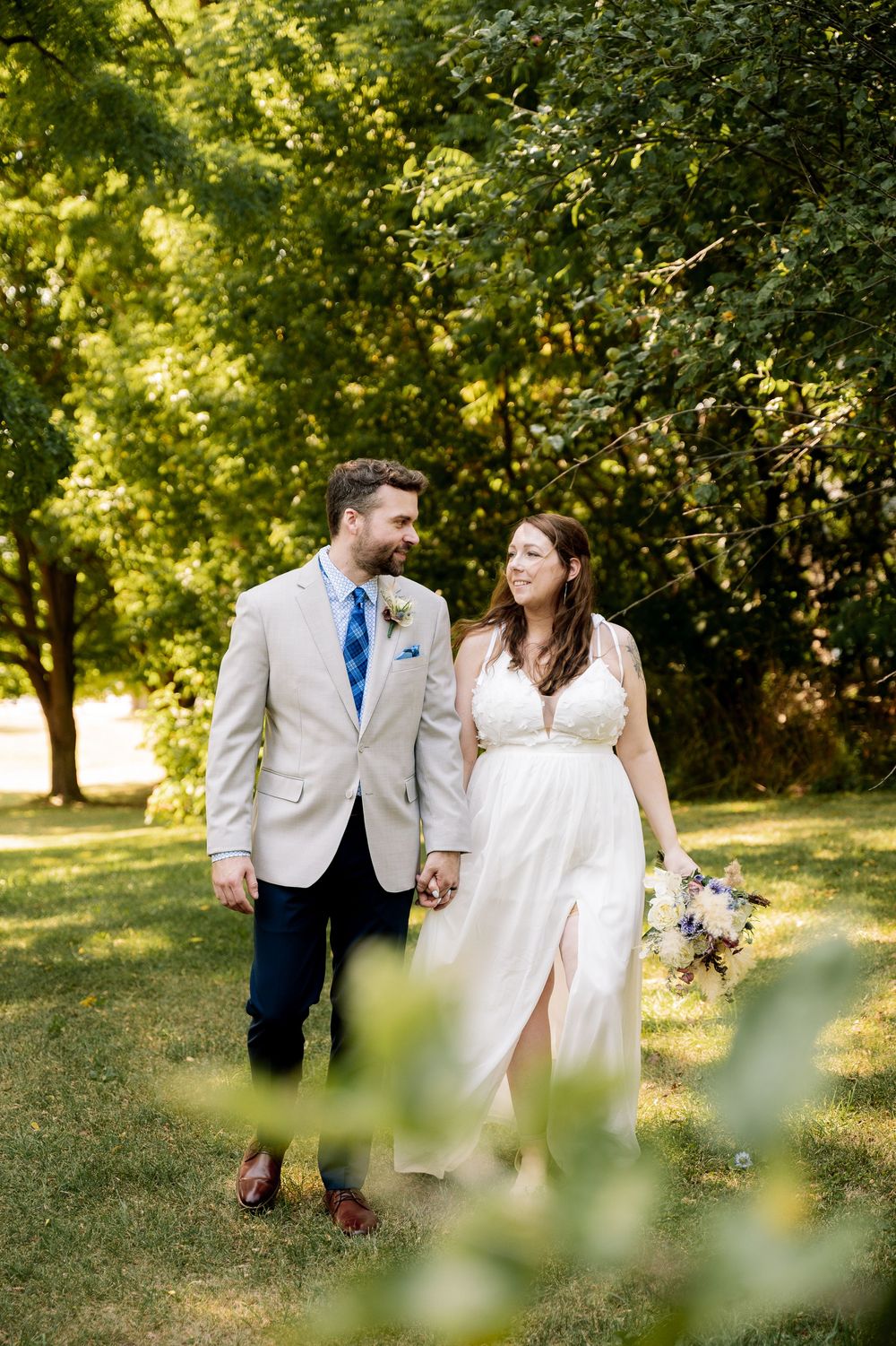 A couple shares romantic moments in a sunlit garden setting wearing white and beige formal attire.