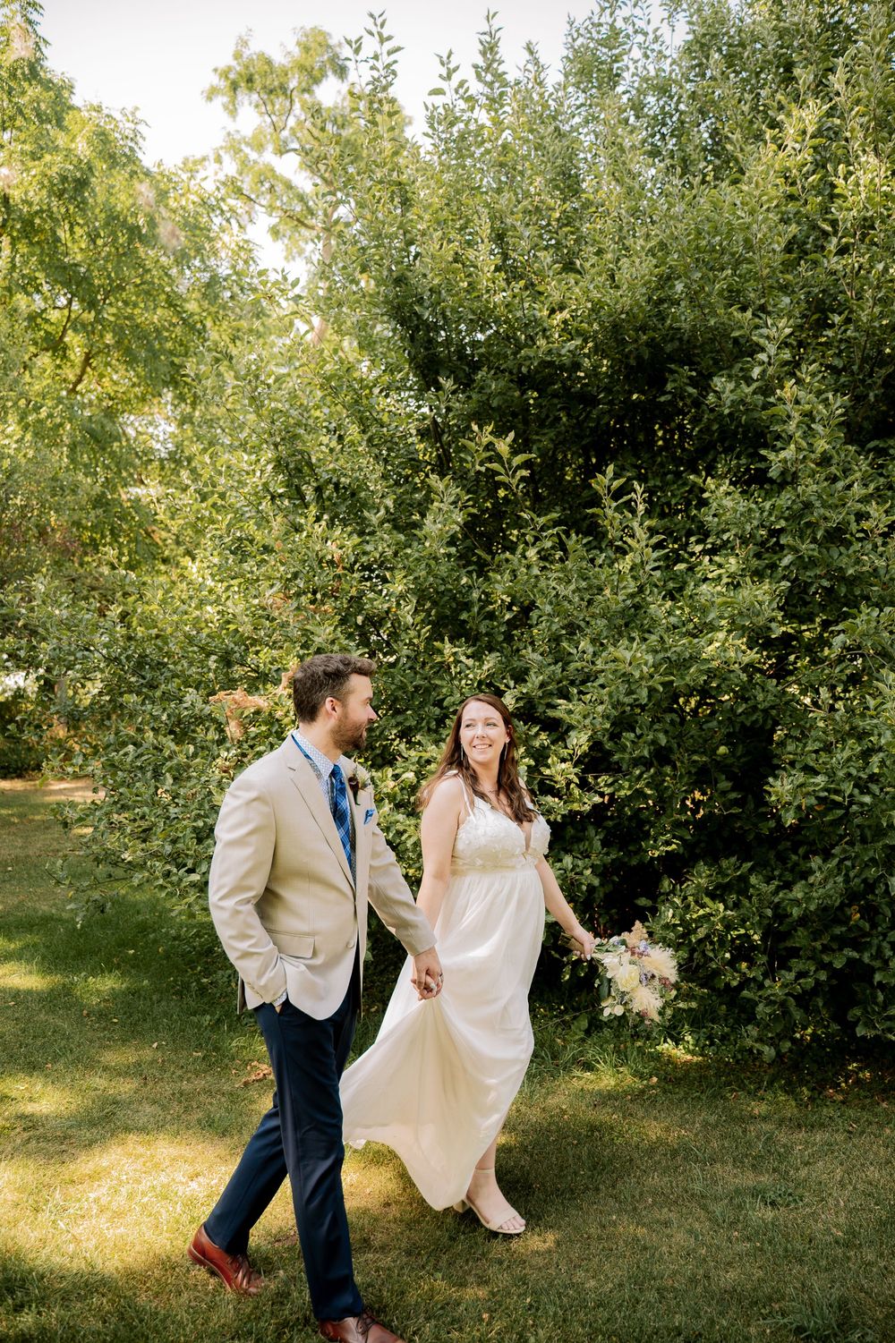 A couple shares a playful moment dancing together in a sunlit orchard on their wedding day.