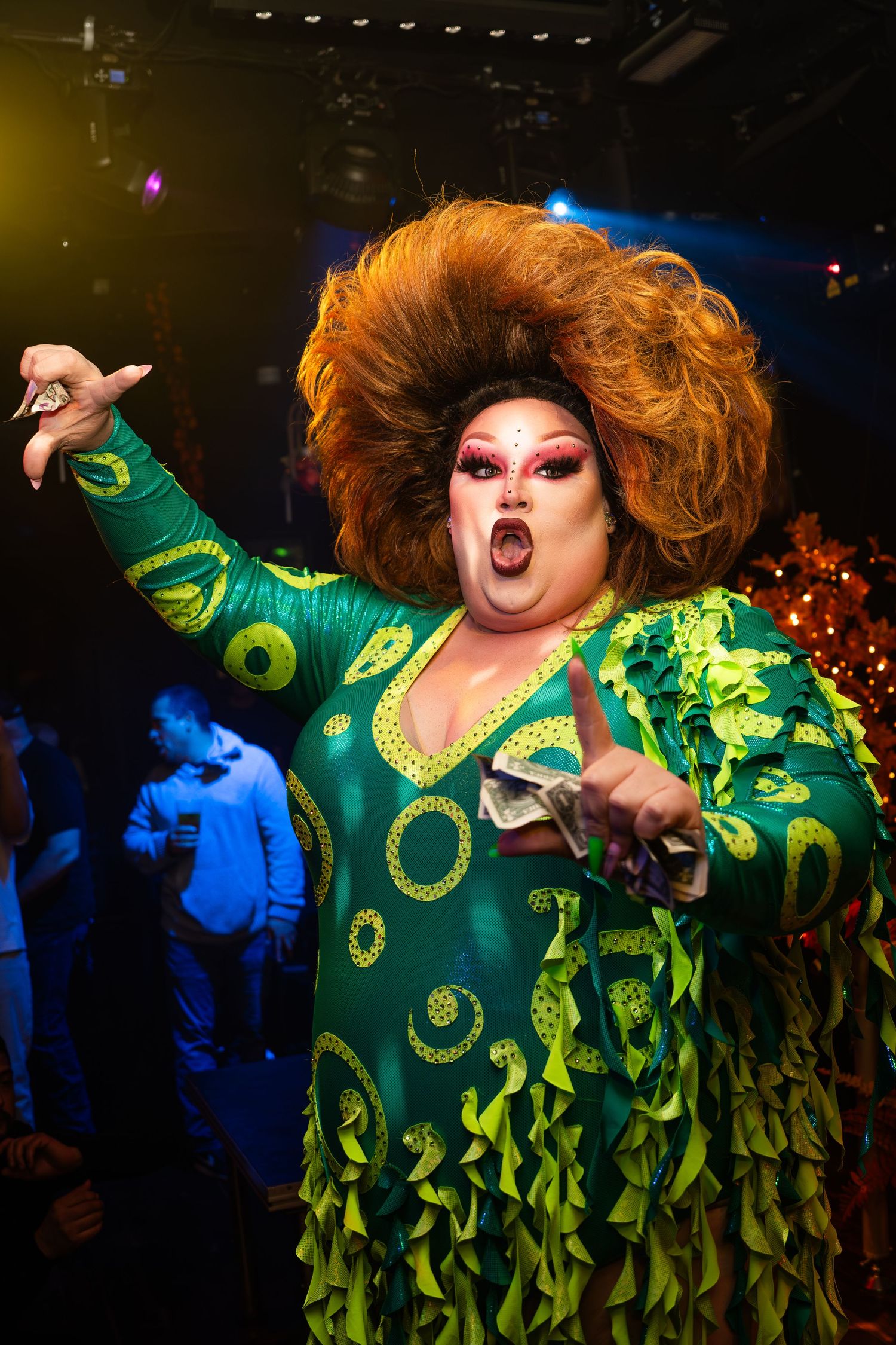looks into the crowd while performing in the tallest wig ever and a peacock inspired dress
