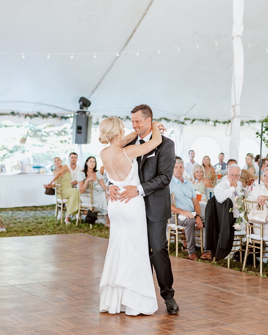Couples dance together under a white tent during an outdoor wedding reception.