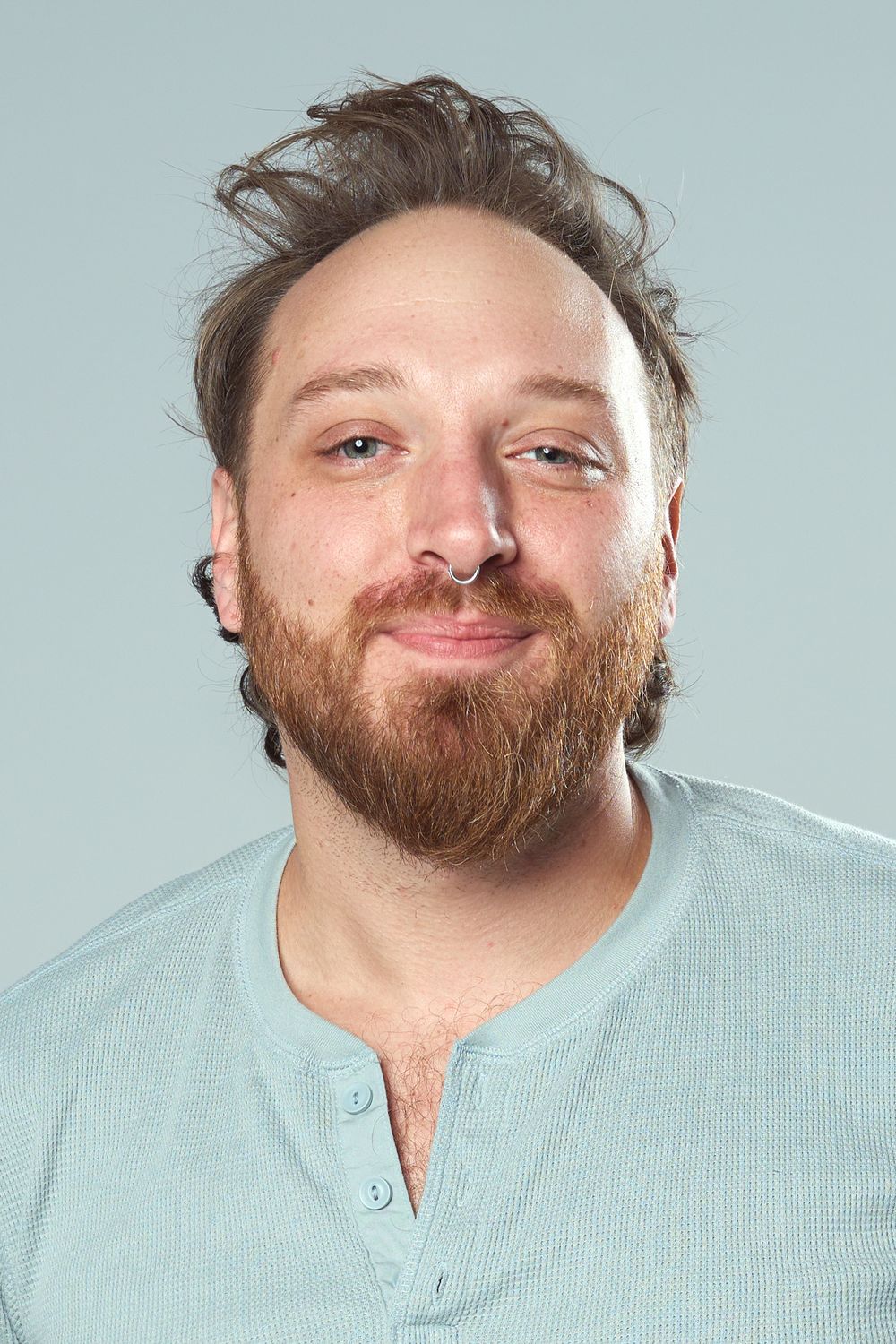 Professional headshot of person with a reddish beard wearing a light colored henley shirt against a blue background.