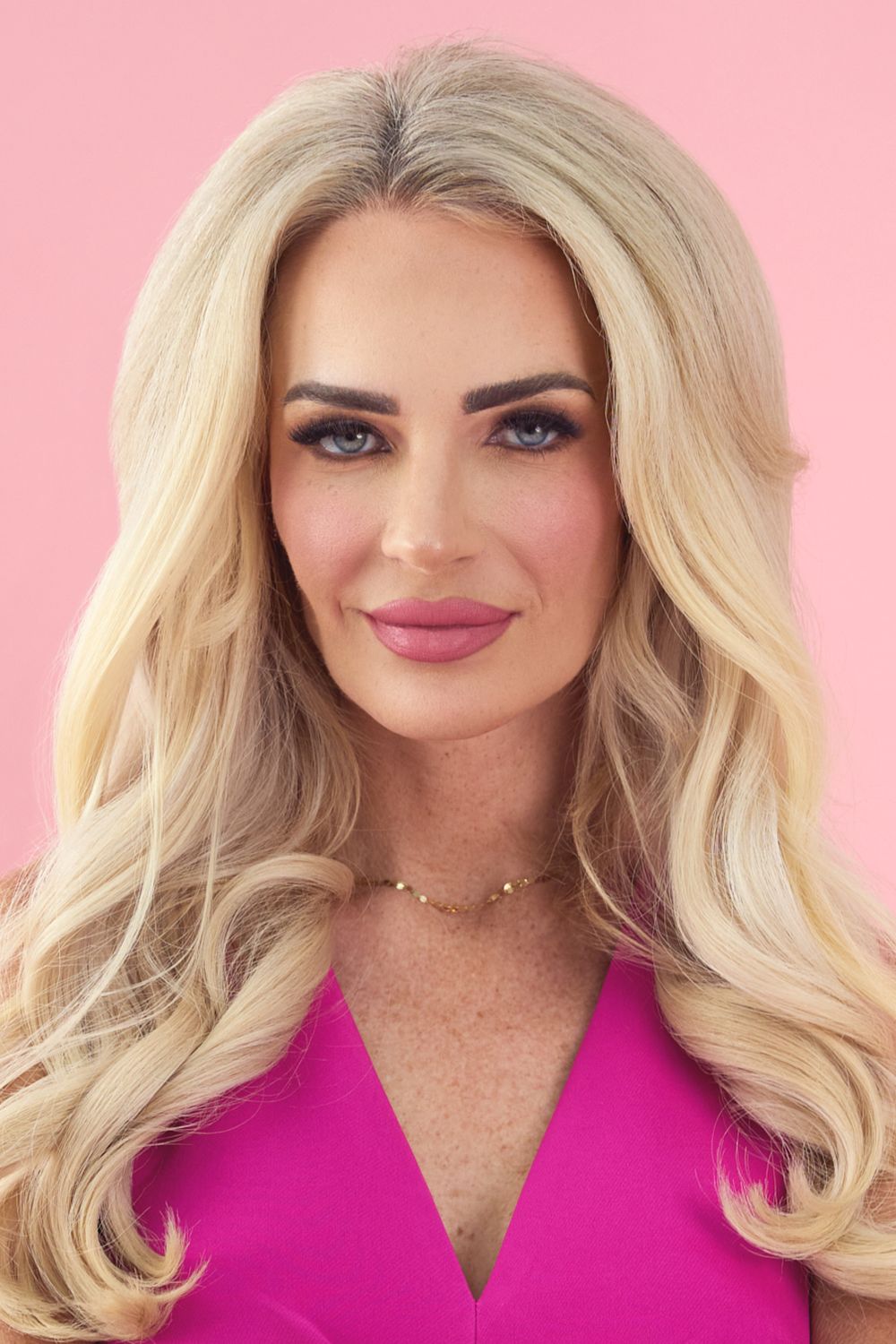 Professional headshot of person with blonde hair and pink lipstick against a pink background.