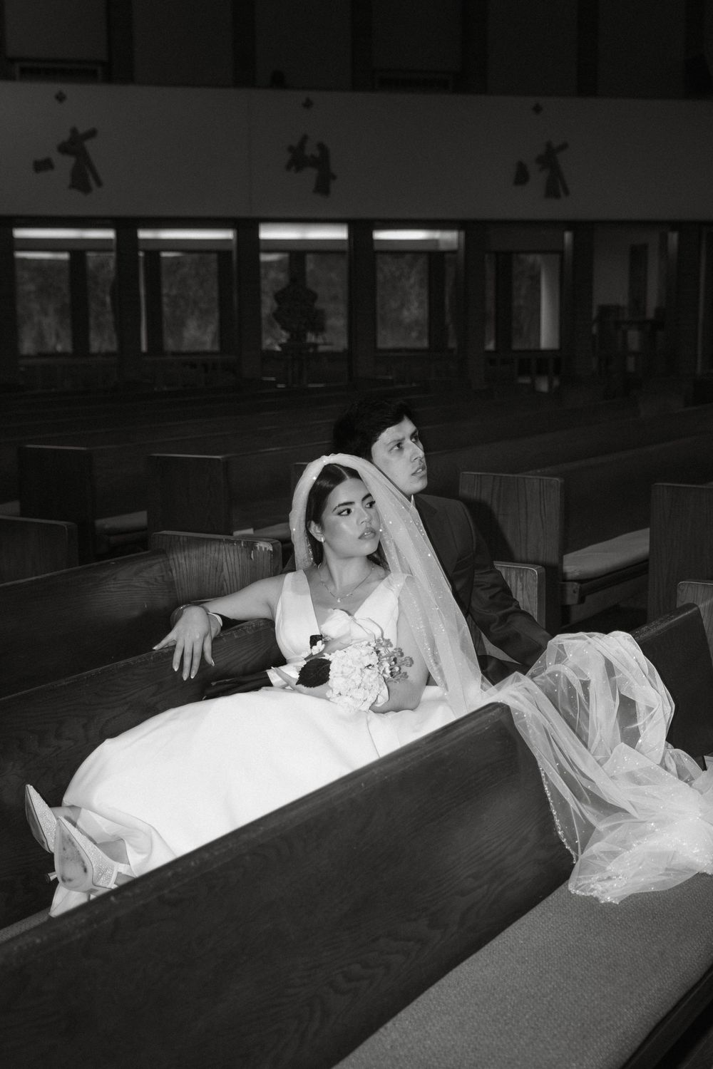 Artistic black and white photo of bride reclining on church pew.