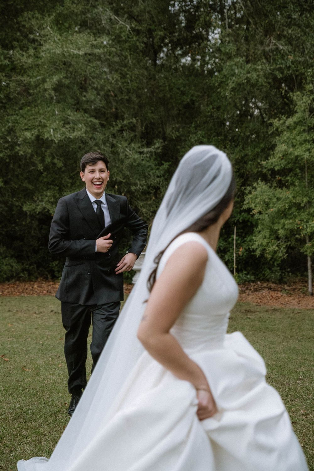 A wedding couple shares a playful moment outdoors as the bride's white dress flows in the breeze.