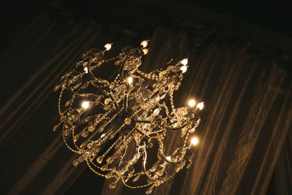 An elegant crystal chandelier illuminates a dark room with warm glowing lights and ornate decorative details.