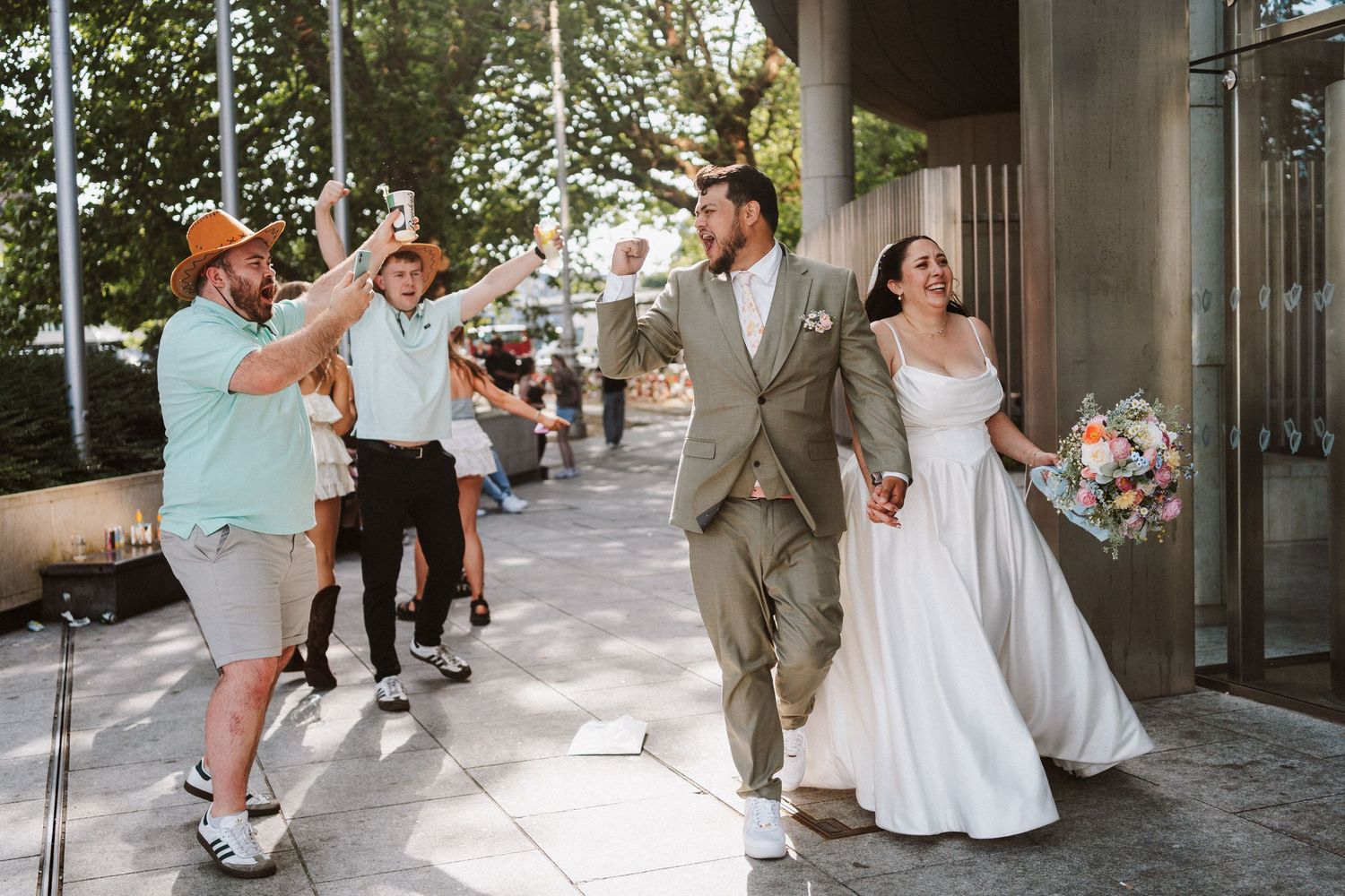Wedding party poses joyfully together in a series of candid outdoor celebration shots along a tree-lined walkway.