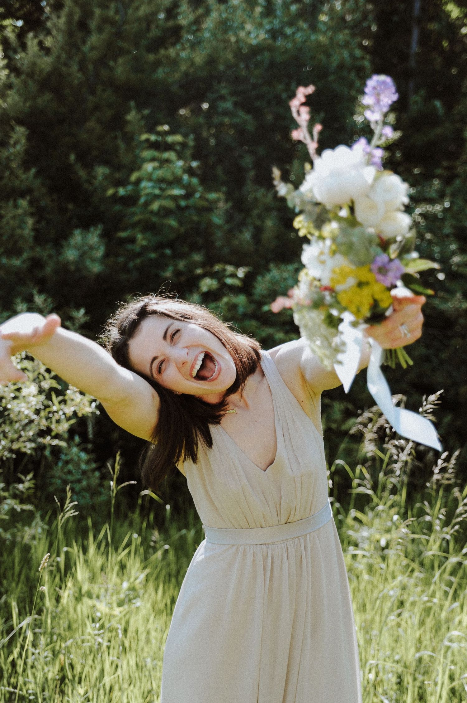 A joyful person in a white dress spins and dances in a sunny meadow surrounded by wildflowers and greenery.