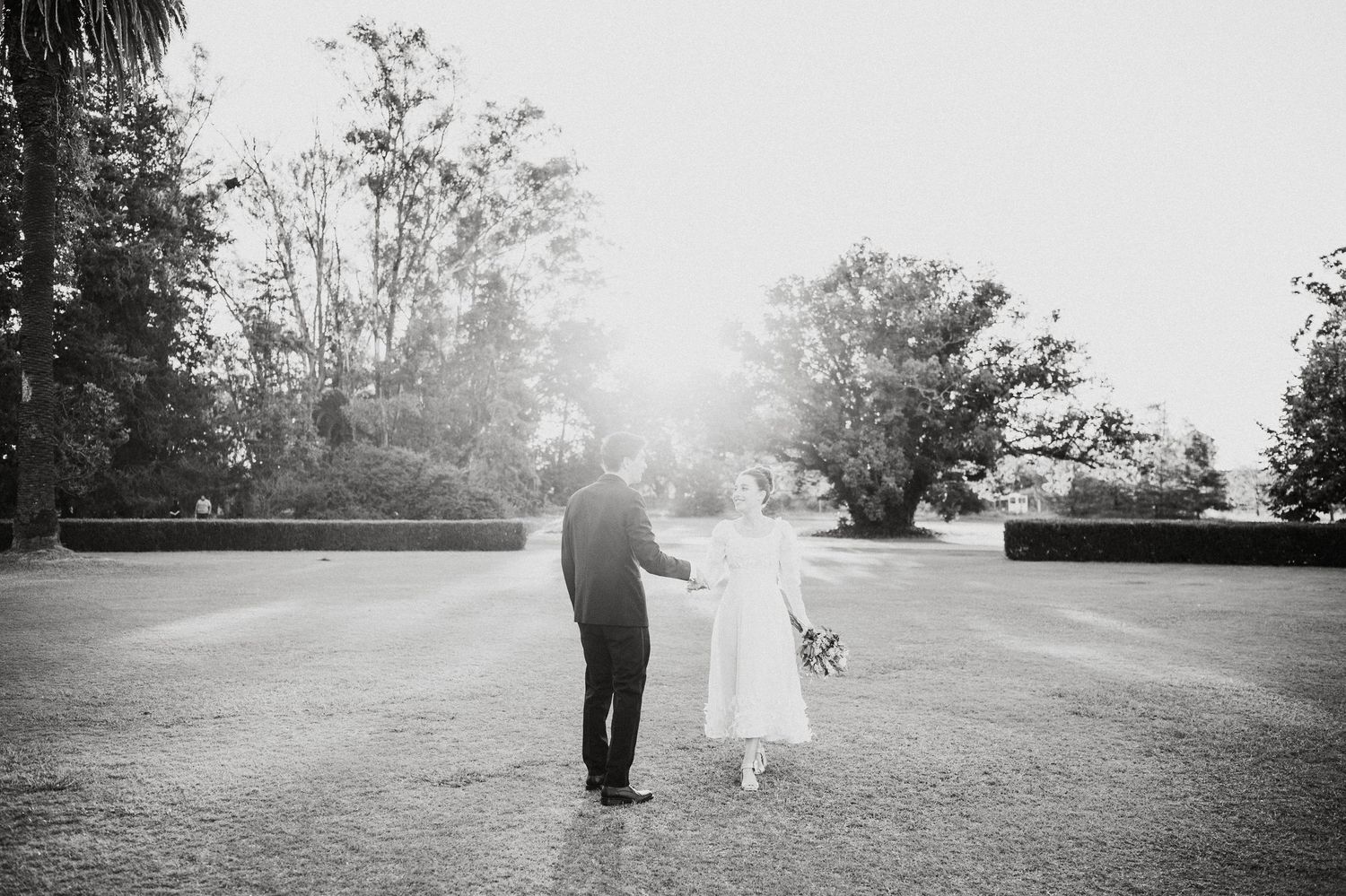 Black and white photo of couple walking through park landscape with dramatic lighting.