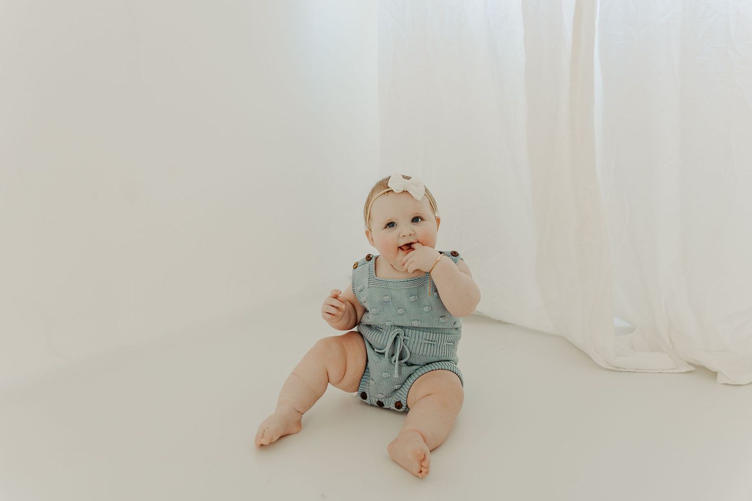 Baby in beige overalls playing with toy truck on white background.