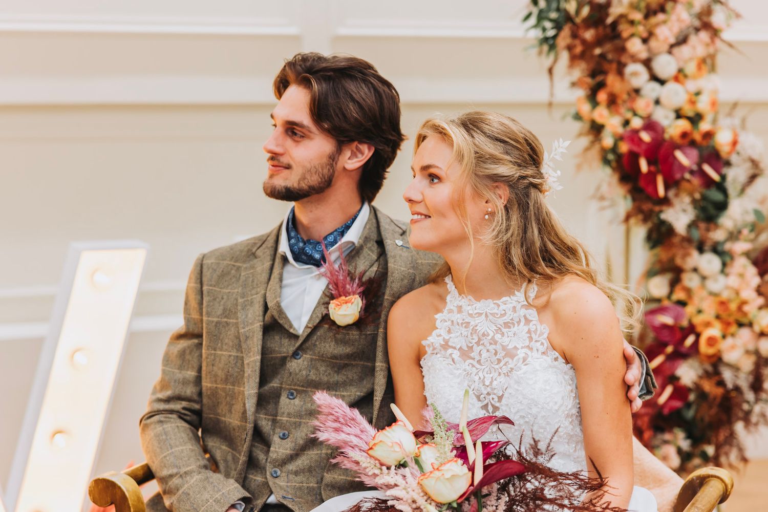 Bride and groom sit at elegant reception table decorated with autumn floral arrangements in warm fall colors.