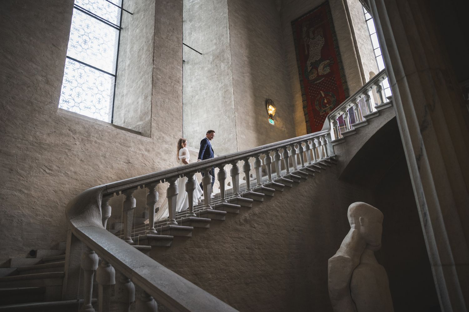 People walking up a spiral staircase inside a historic stone tower with dramatic lighting and white walls.