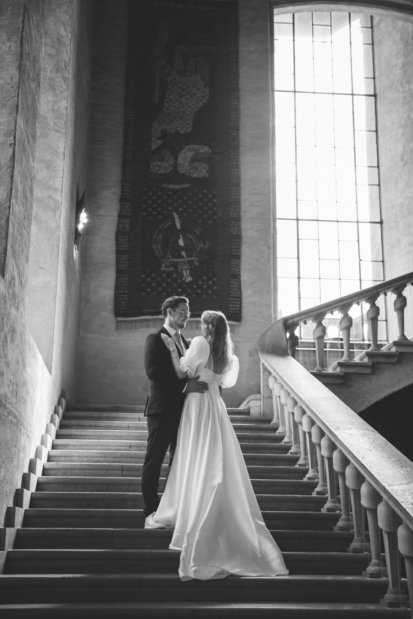 A series of black and white wedding photos showing a couple ascending elegant marble stairs in a grand building.