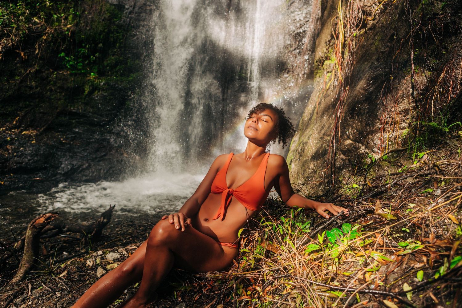 Solo photo session, a woman basking in the sun in front of a waterfall with a rainbow behind her, in Vilcabamba Ecuador