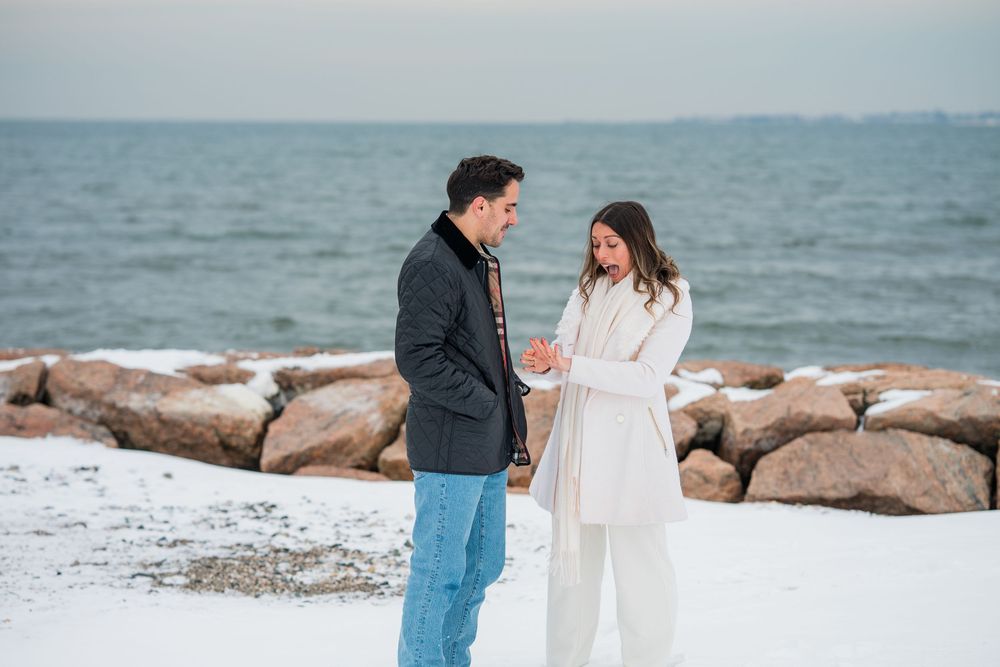 Two people share an intimate moment on a winter beach with rocky shoreline.