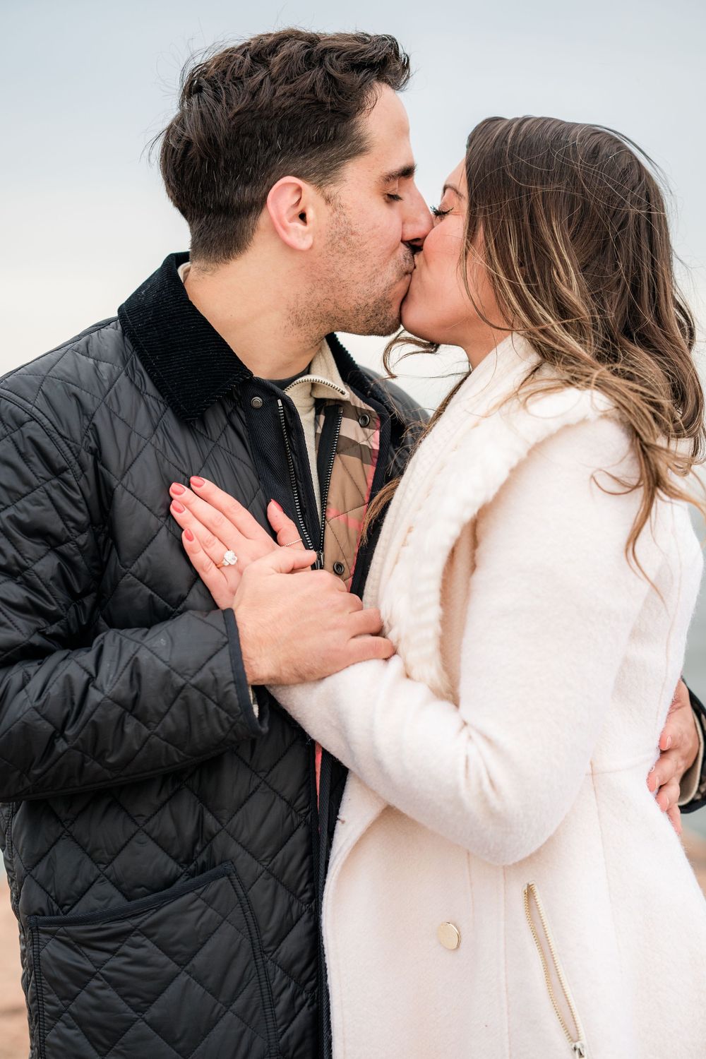 A couple shares a romantic kiss while wearing winter coats in a series of intimate outdoor photos.