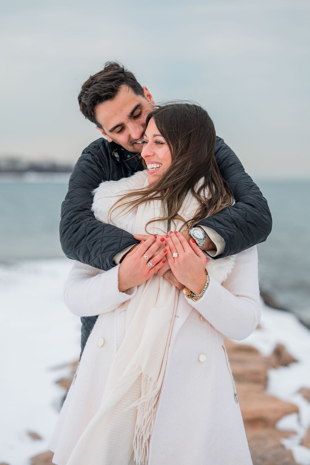 A couple embraces warmly on a snowy beach during winter, wearing coats against the cold weather.