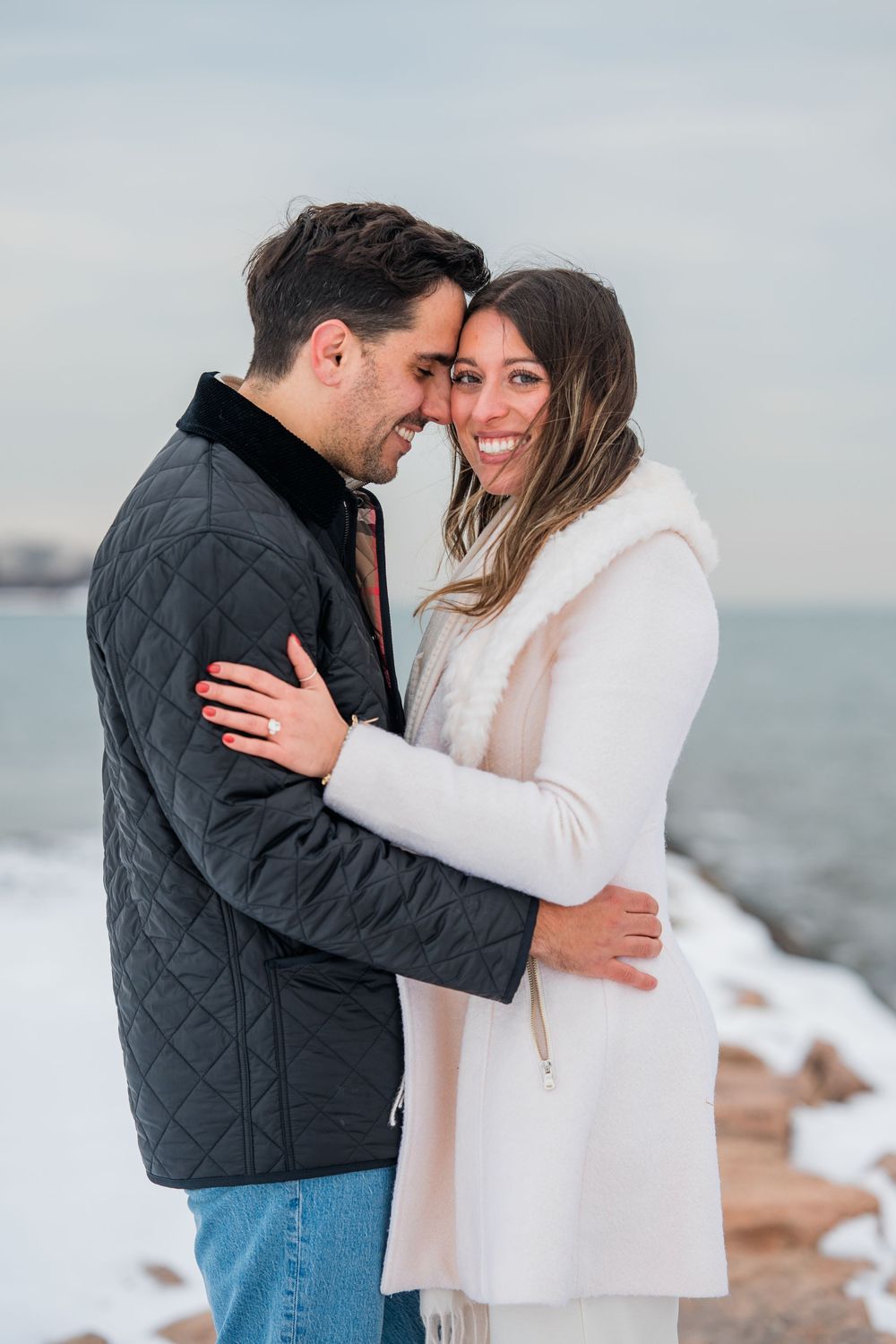 A romantic winter beach scene shows a couple sharing an intimate moment in warm coats by the water.