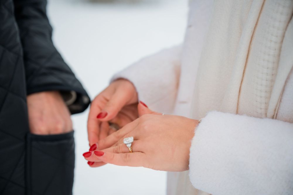 Close-up shot of hands exchanging an engagement ring during a beach proposal.