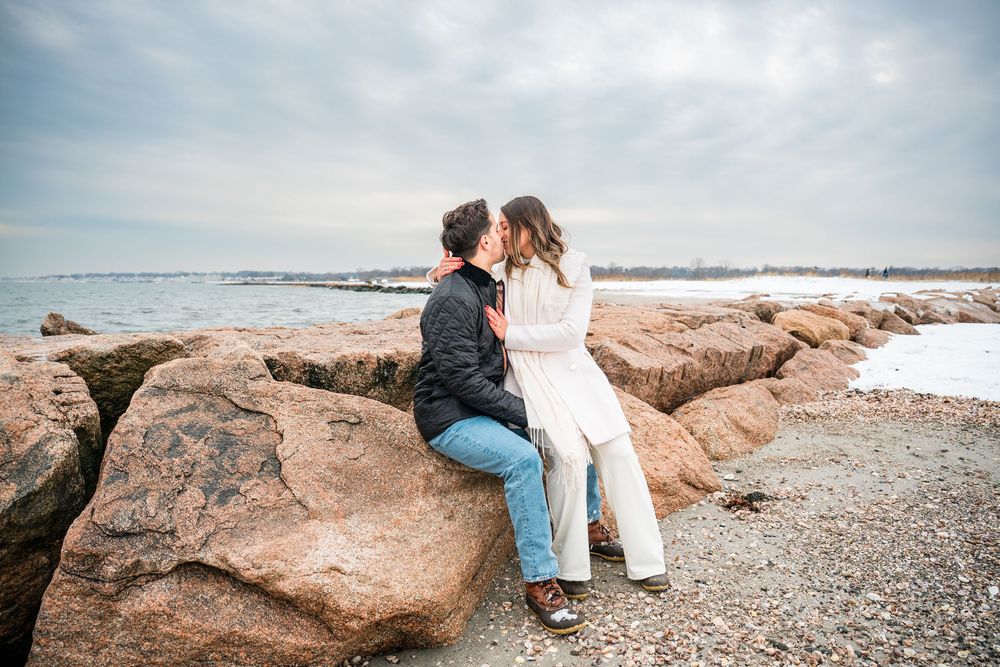 Two people walk along a rocky beach coastline during an overcast winter day.