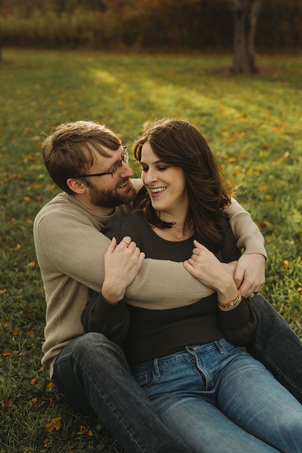 A couple in casual clothing shares tender moments while sitting on autumn grass surrounded by fallen leaves.