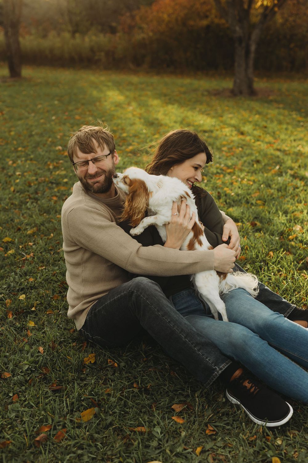 A couple relaxes on autumn grass with their playful Jack Russell Terrier dog during a cozy outdoor photo session.