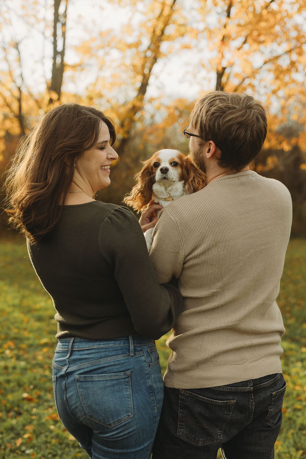 Couple in casual attire embraces while enjoying an autumn day with golden leaves falling in the background.
