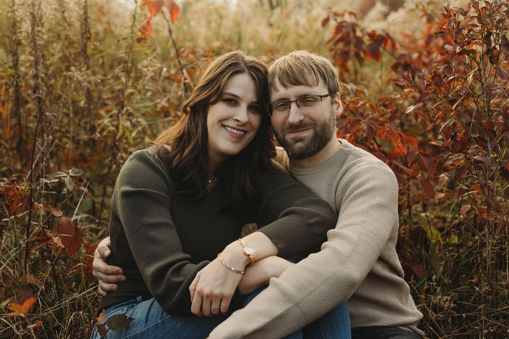 A couple embraces while posing in front of autumn foliage during a romantic outdoor photoshoot.