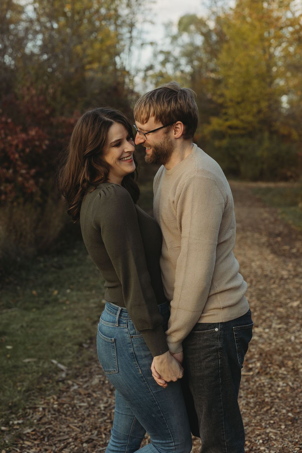 A couple shares an intimate moment outdoors during autumn, wearing casual sweaters and jeans while holding hands.