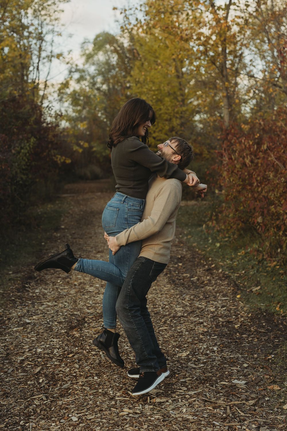 A couple playfully spins and dances together on a woodland path during autumn.