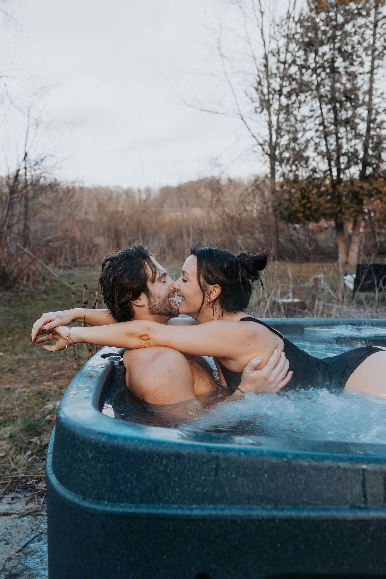 Couple sharing an intimate moment in an outdoor hot tub surrounded by fall foliage.