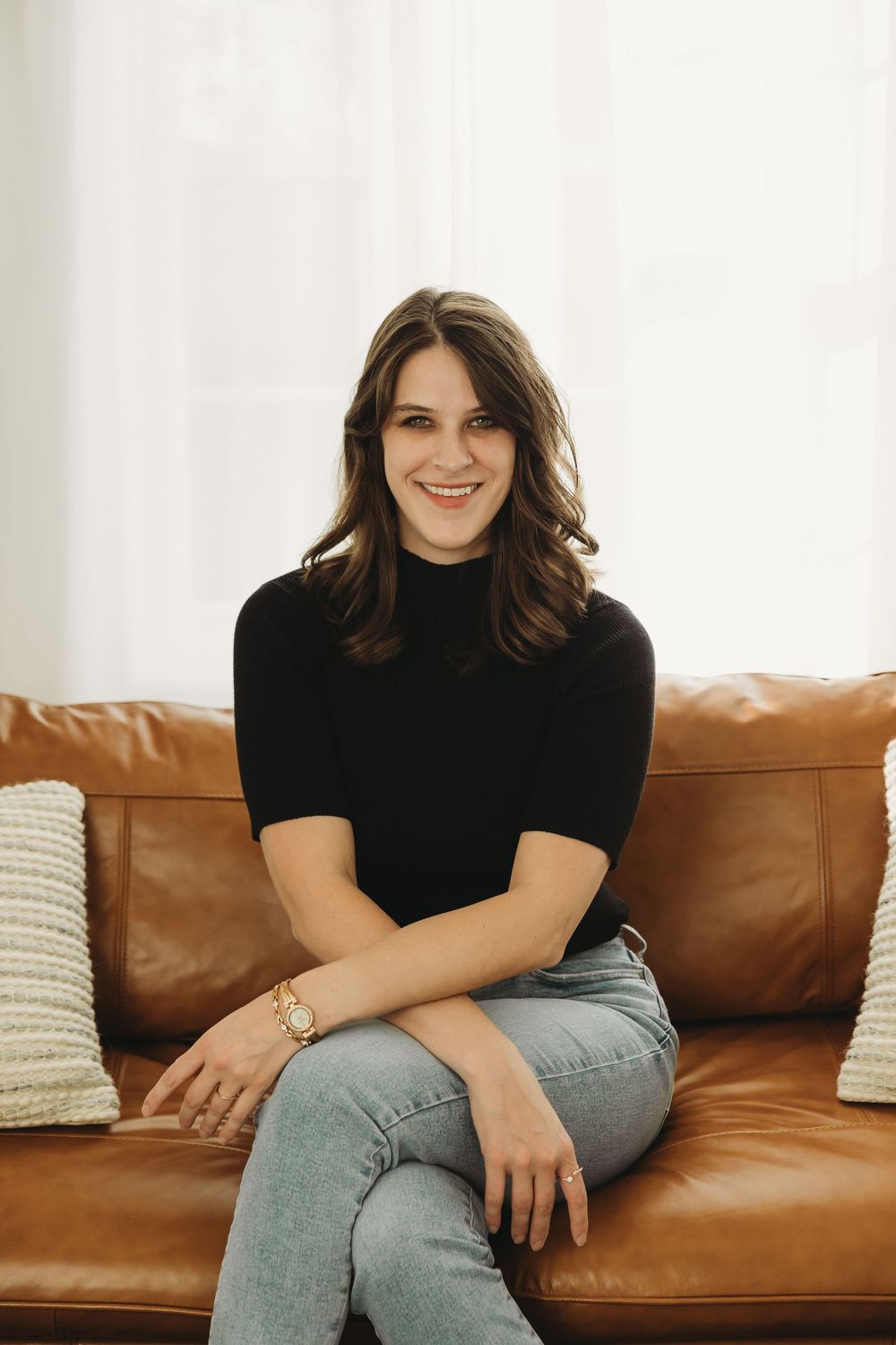 Person wearing black turtleneck and jeans relaxes on brown leather couch in casual lifestyle photoshoot.