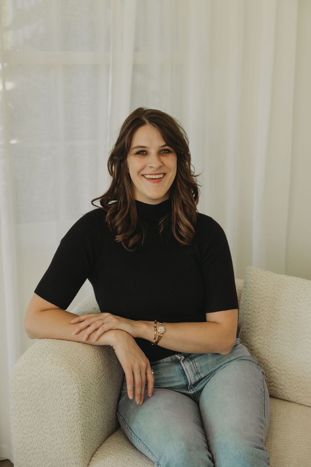 A person in a black t-shirt and jeans sits casually on a cream-colored couch in a series of relaxed poses.