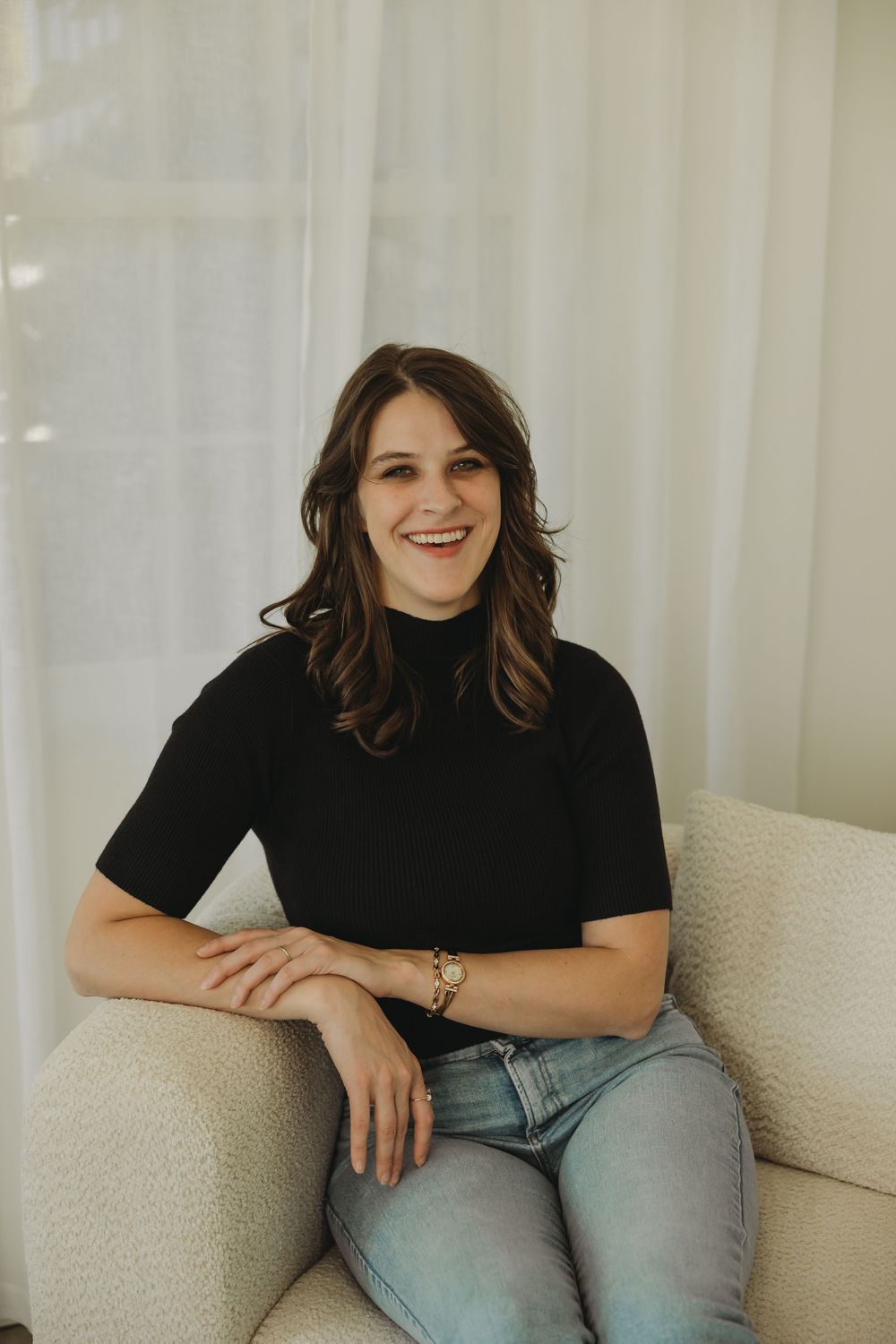 A person wearing a black shirt and jeans sits casually on a white couch in a series of candid poses.