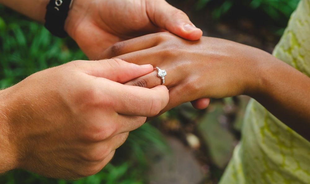 Close-up sequence of hands exchanging a diamond engagement ring during a romantic outdoor proposal.