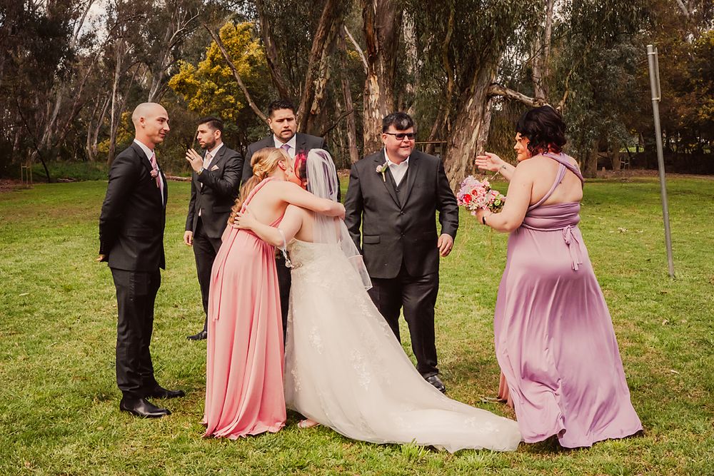 Wedding party poses together in a lush garden setting with bridesmaids in pink dresses and formal attire.