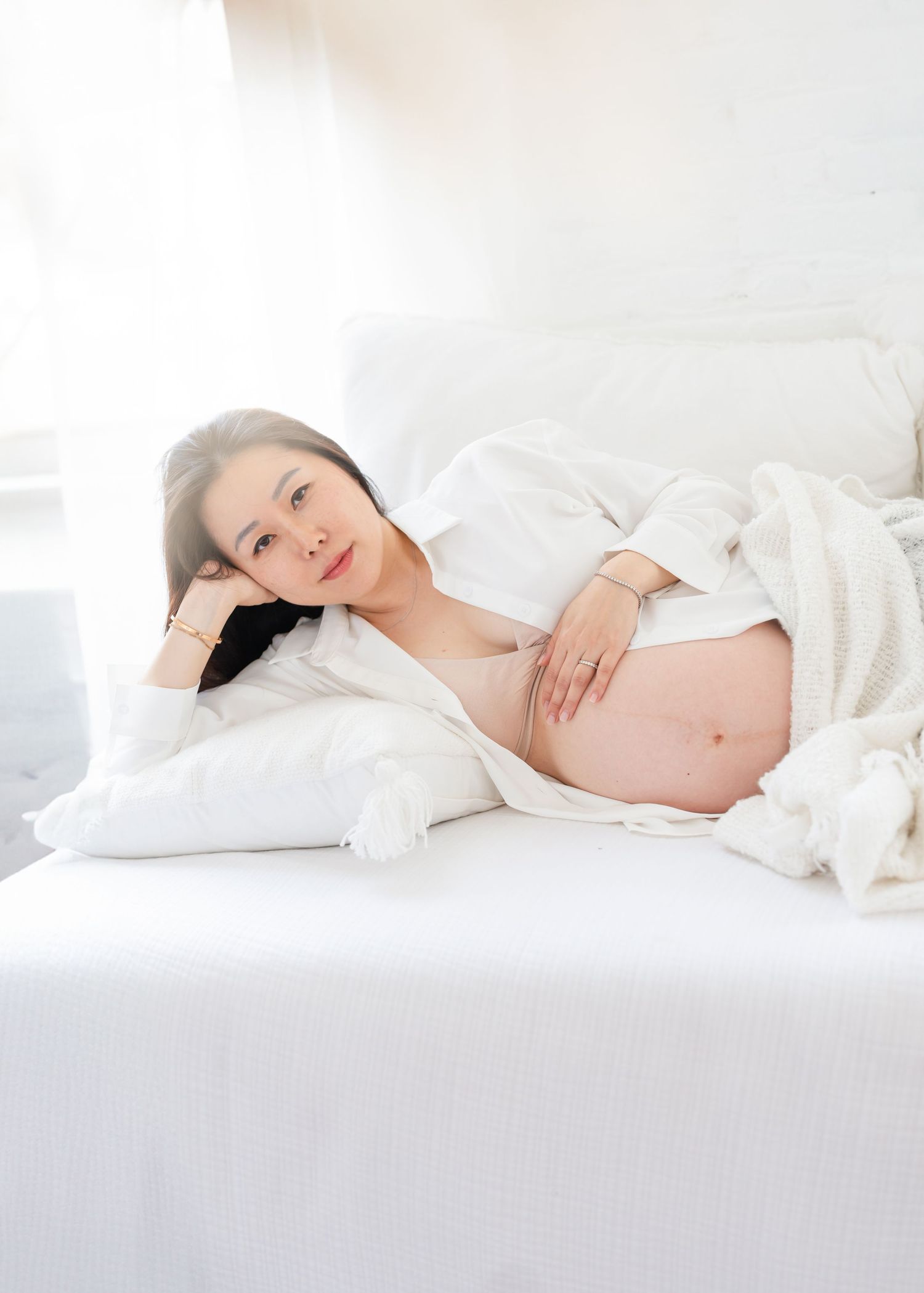 A sleeping newborn baby lying on white bedding while being gently held by adult hands.
