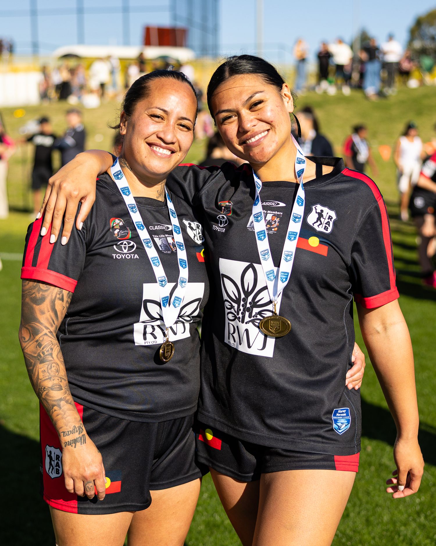Rugby teammates in black jerseys celebrate together on sunny field.