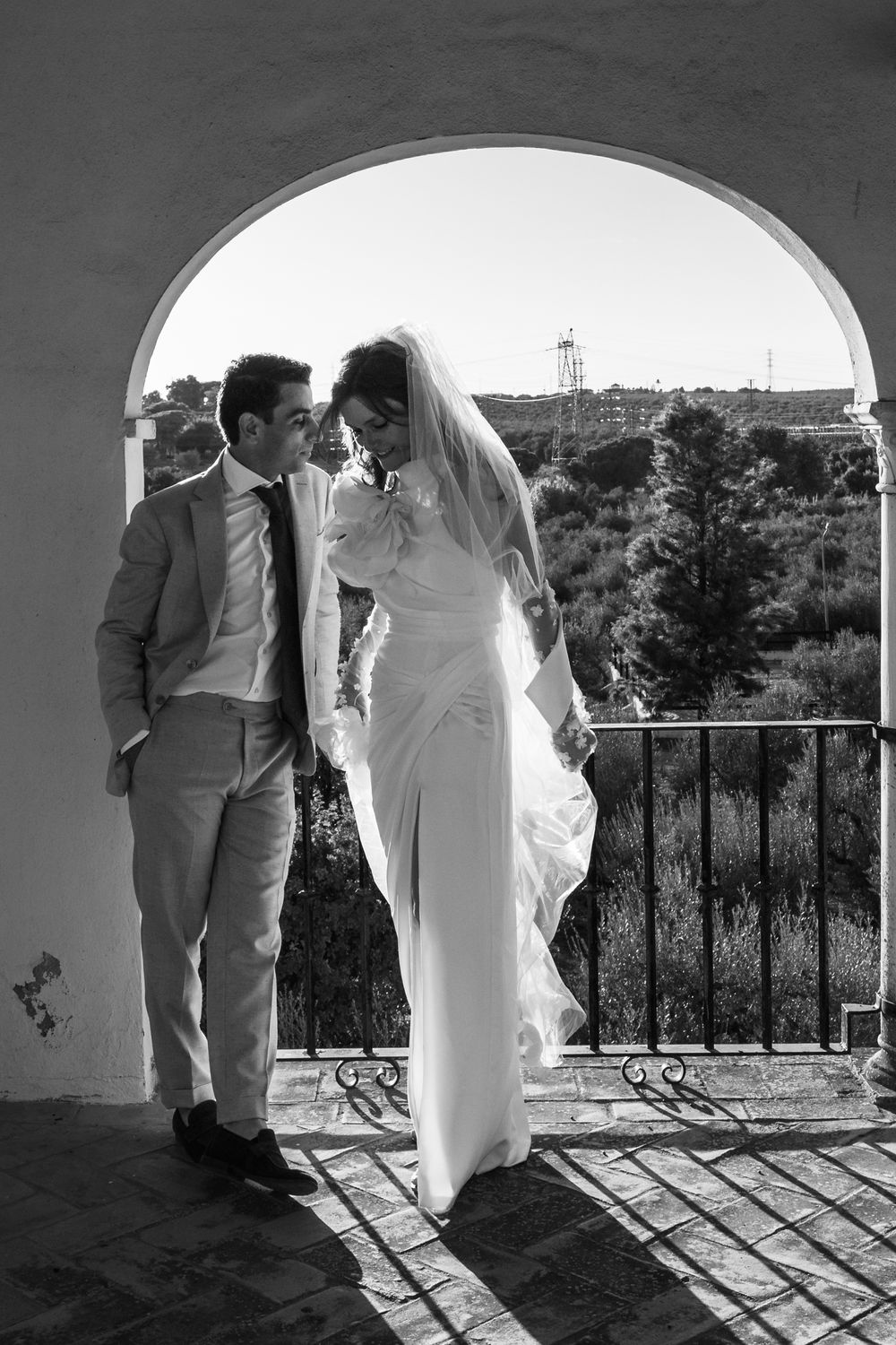 A romantic black and white photo series showing a couple in wedding attire standing in an arched doorway overlooking scenery.