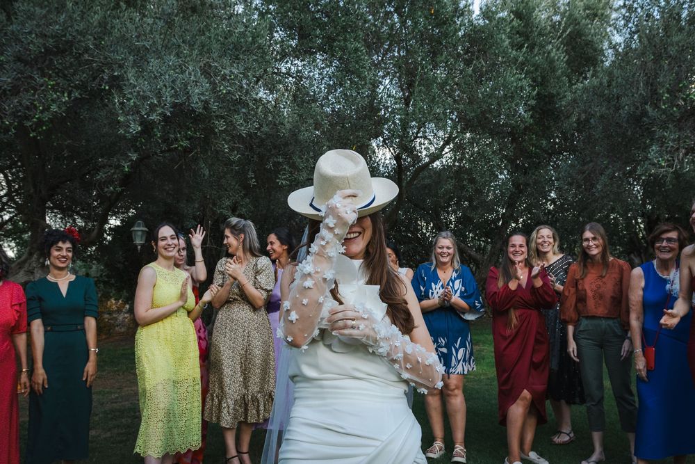 Wedding guests celebrate outdoors during a group photo session under trees in a garden setting.
