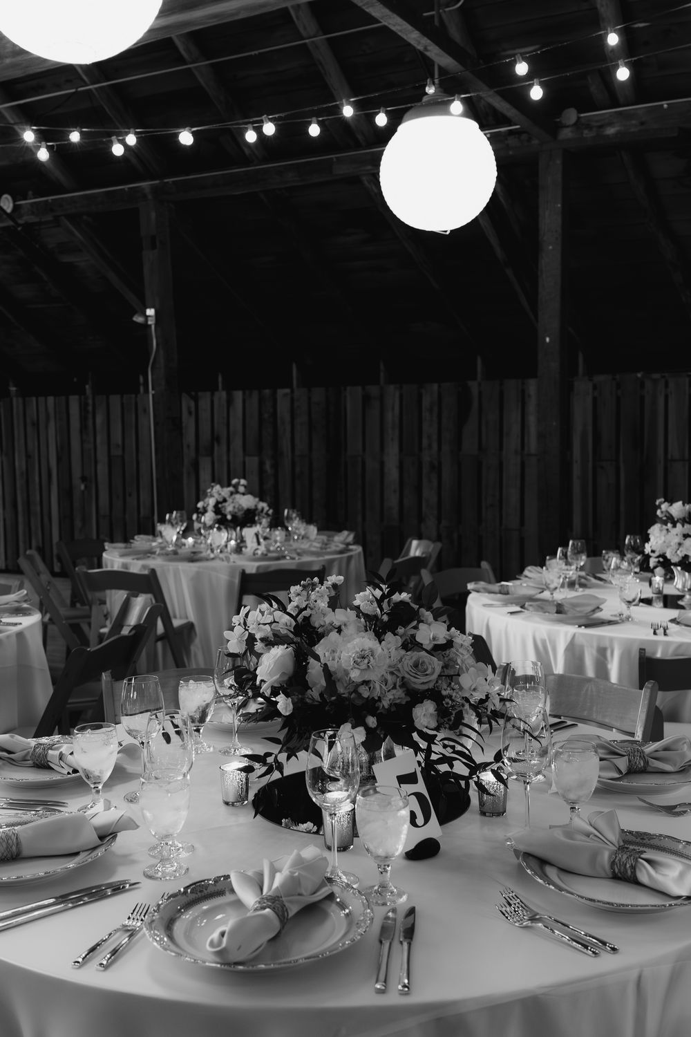 Elegant wedding reception tables set with white linens, round paper lanterns, and ambient lighting in a rustic venue.