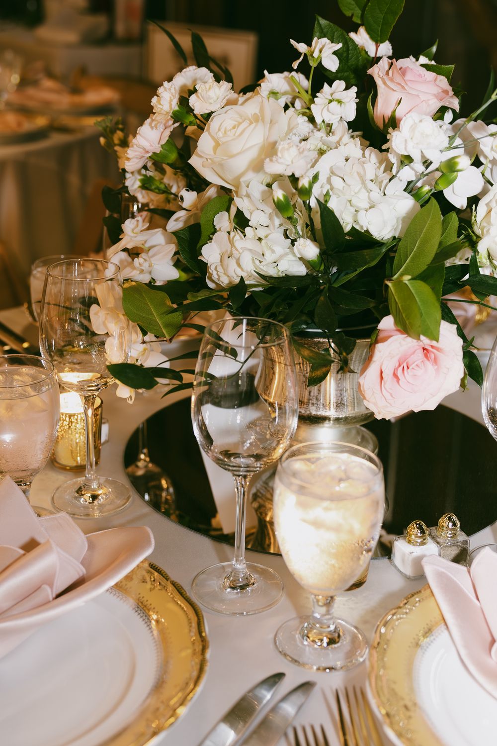 Wedding table settings with gold chargers, white flowers, and glowing candles creating an intimate atmosphere.